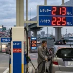「レギュラー213円、ハイオク225円と200円を超えた価格を表示するガソリンスタンドの看板と、車に給油する男性。ガソリン価格高騰の将来予測イメージ」