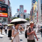 「気温40.8℃を記録した2026年夏の東京・渋谷スクランブル交差点。エルニーニョ現象による猛暑の中、日傘や携帯扇風機で暑さ対策をして歩く人々。」